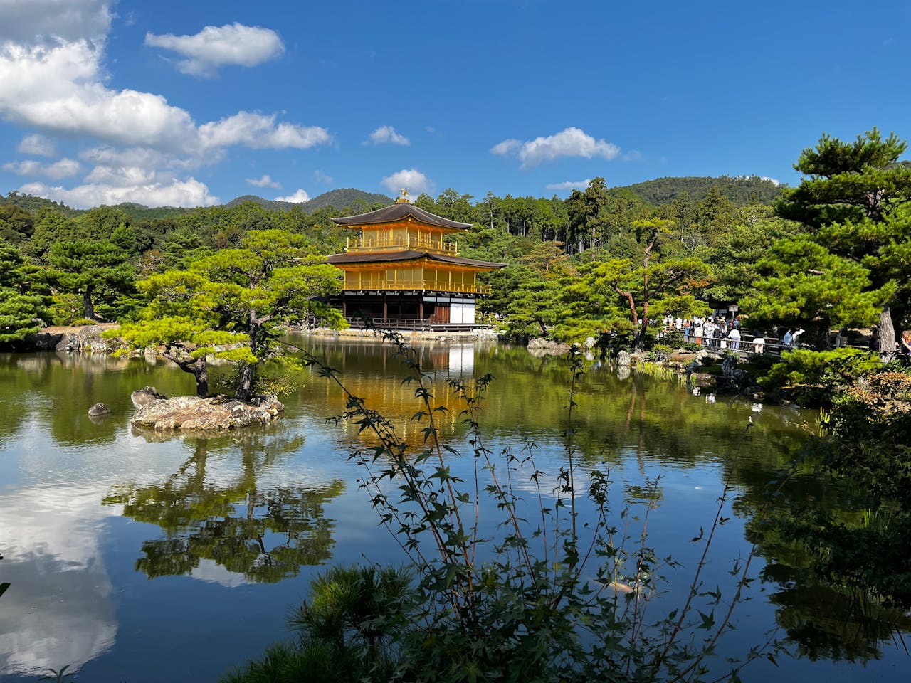 Scenic view of Kinkaku-ji Temple in Kyoto reflecting in a serene pond under a clear blue sky.